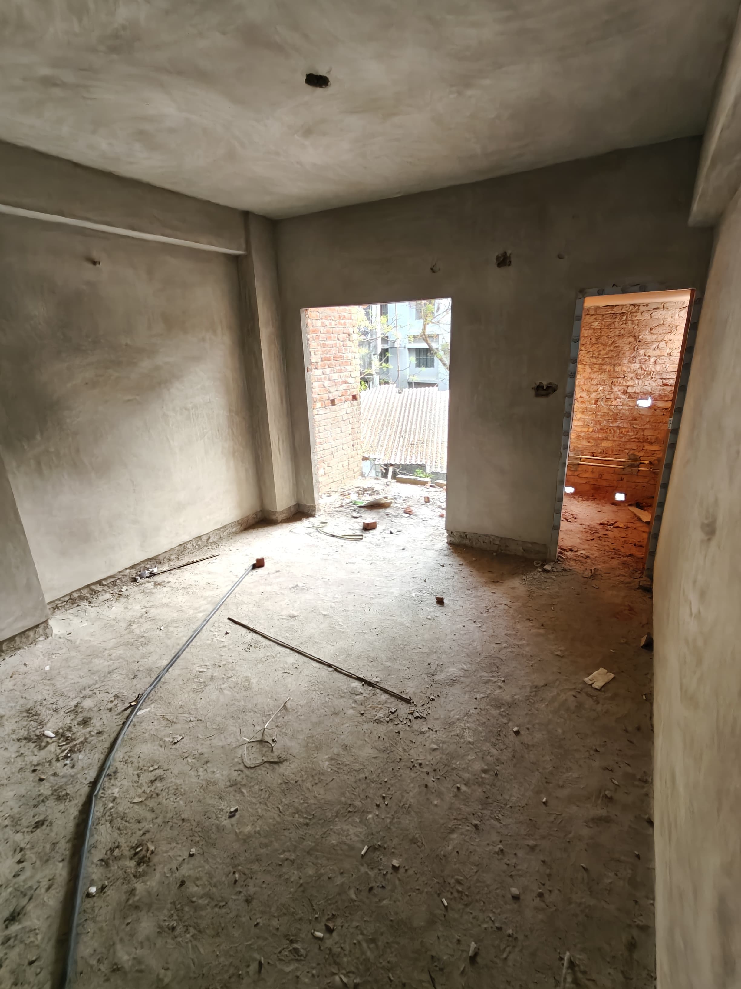 Unfinished concrete room with debris on the floor and openings showing exposed brick walls.