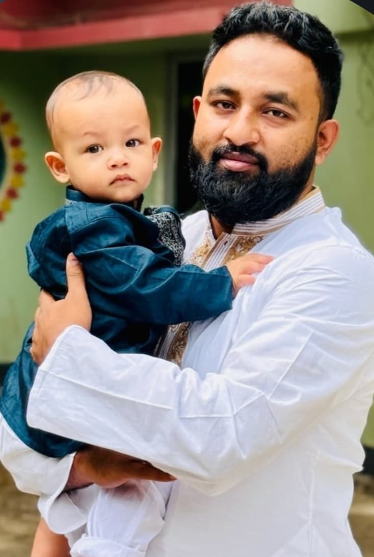 Bearded man in a white kurta holding a baby wearing a blue traditional outfit.